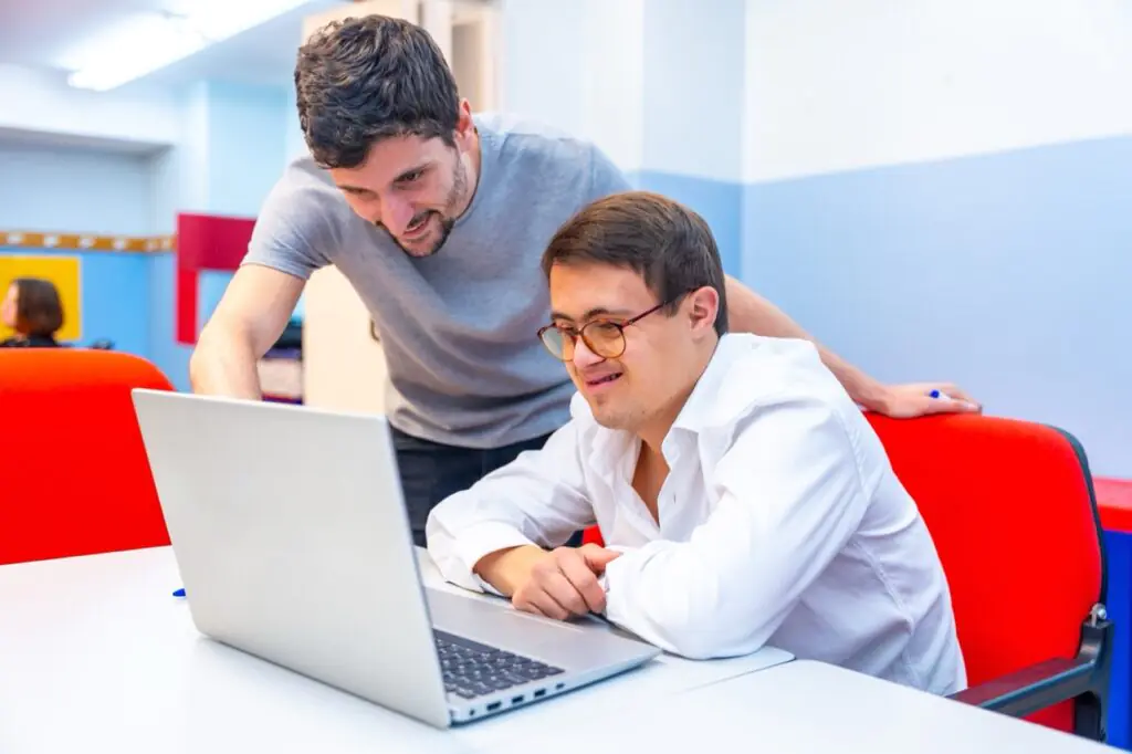 Direct support professional helping a man work on a laptop, part of the IDD workforce